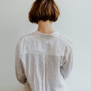 A person with short brown hair is wearing a long-sleeve white linen shirt and standing against a white background.