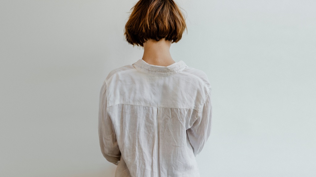 A person with short brown hair is wearing a long-sleeve white linen shirt and standing against a white background.
