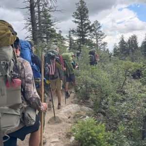 Troop 321 is shown backpacking at Philmont Scout Reservation. The Crew Chief in the middle of the column, Life Scout Nate Pyron, carries the traditional American flag carried by Philmont Crew Chiefs. This tradition has been in place since the beginning of Philmont and has been observed by astronauts and statesmen who have hiked the same rugged mountains.