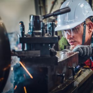 A mechanical engineer wearing safety gear operates a lathe machine for metalwork and supervises its operation.