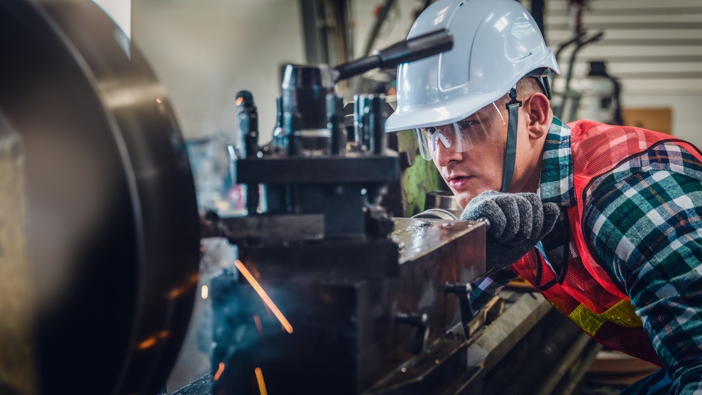 A mechanical engineer wearing safety gear operates a lathe machine for metalwork and supervises its operation.
