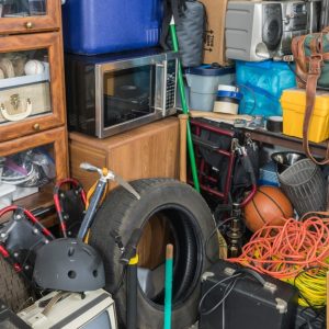 A cluttered garage full of various items, including a tire, a basketball, a helmet, a skateboard, a microwave, and more.