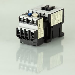 A black and white electrical contactor sits on a shiny and reflective cream-colored surface. It has two stickers on the side.