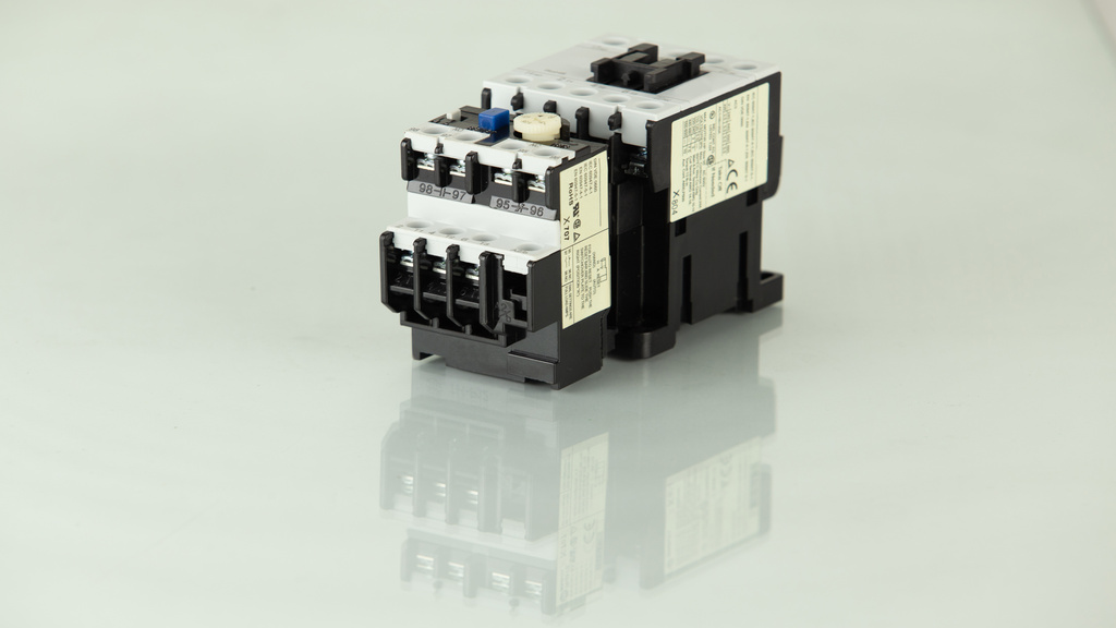 A black and white electrical contactor sits on a shiny and reflective cream-colored surface. It has two stickers on the side.