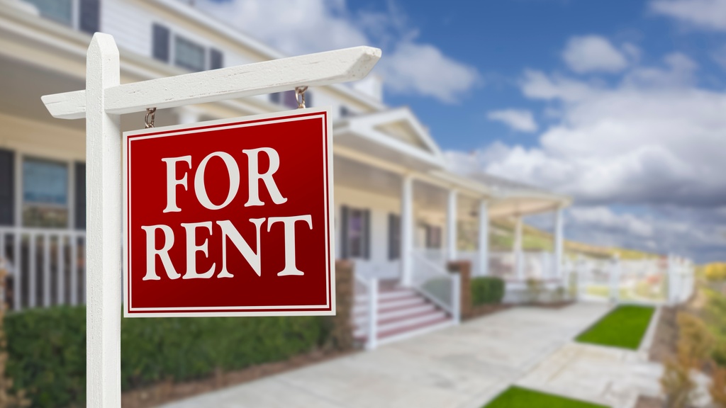 A red "For rent" sign in the front of a rental property. The sidewalk is groomed with a white porch and cement steps.