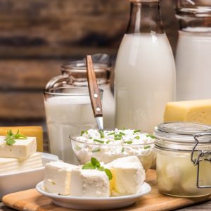 A collection of dairy products sit on a wooden table. The products range from milk, cheddar cheese, and cottage cheese.