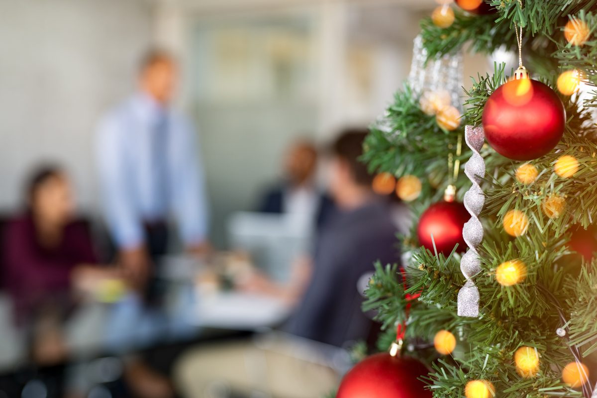 A close-up view shows a Christmas tree with red balls and silver twisted ornaments. People appear blurry behind the tree.