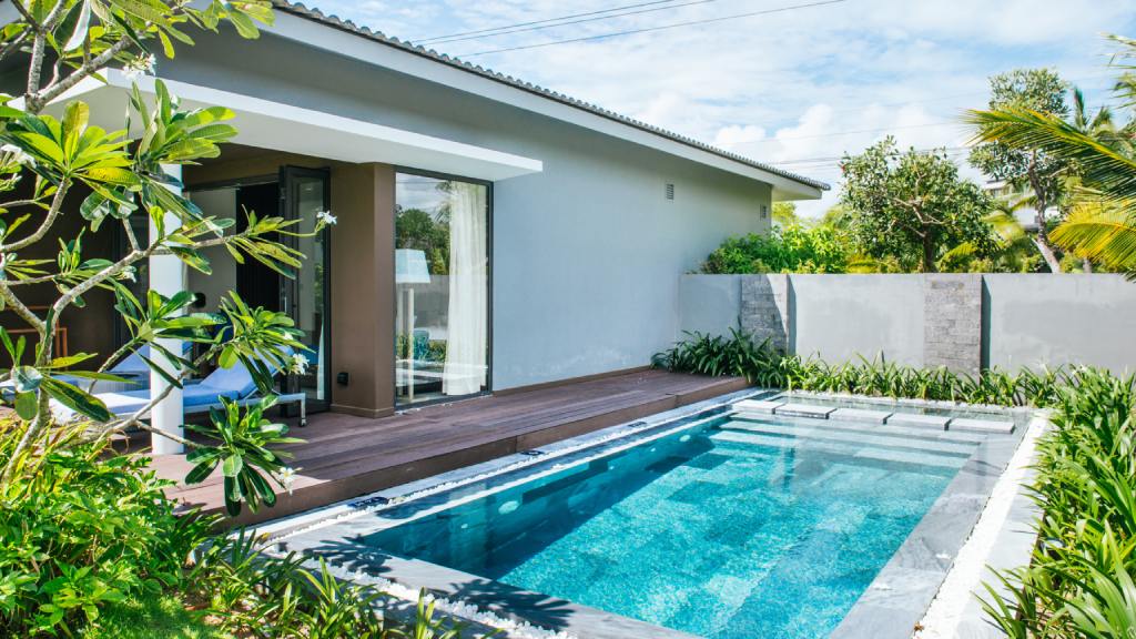 The backyard of a home in a tropical environment with a small, rectangular inground pool with lounge chairs nearby.