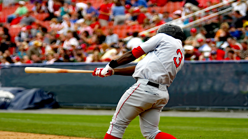 A baseball player wearing a jersey with the number three on the back swings at a baseball right-handed during a day game.