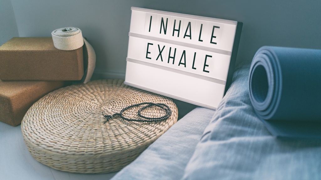A backlit letterboard sign that reads "INHALE EXHALE" alongside various tools for meditation.