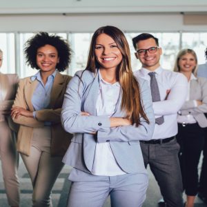A group of people dressed in formal clothes and smiling, standing in an pointed formation inside an office environment.