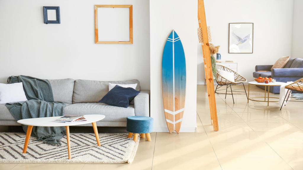 The interior of a home with white walls, empty frames, beach and surfing decor, and modern furniture pieces.