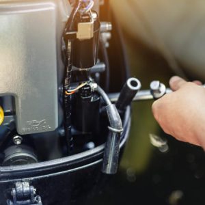 A close-up of a mechanic using a wrench to repair an inflatable motorboat engine at a boat repair garage.