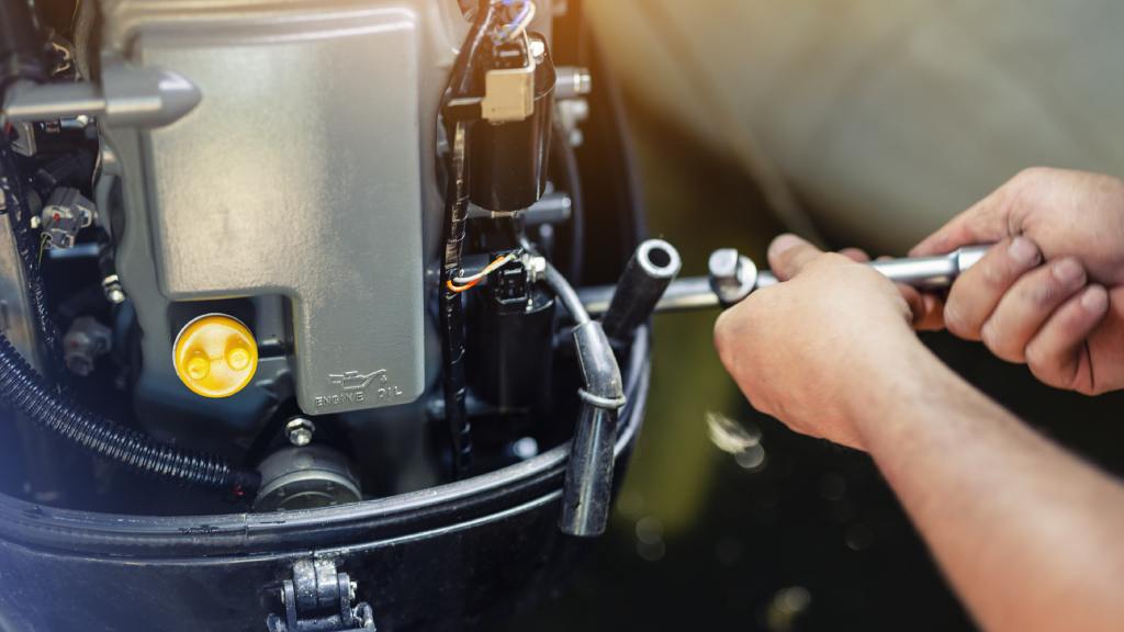A close-up of a mechanic using a wrench to repair an inflatable motorboat engine at a boat repair garage.