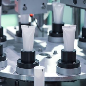An automated machine fills and seals cosmetic plastic tubes on a rotating platform in a high-tech manufacturing facility.