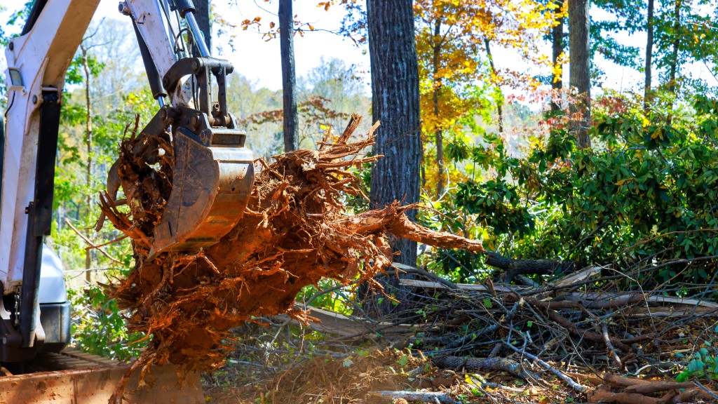 An excavator bucket lifts tree roots and debris on a construction site during land clearing operations.