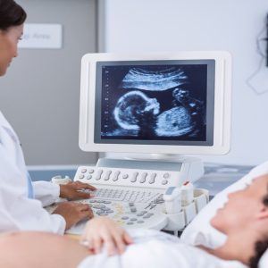 A pregnant woman lies down with her belly exposed while a female healthcare professional looks at the ultrasound machine.