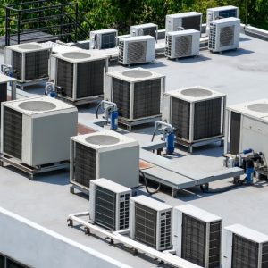A roof of a building has several HVAC systems. There are trees in the back ground in a wooded area near the building.