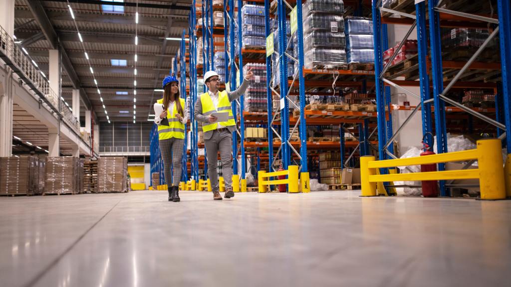 Two managers walking past rows of pallet racking units while pointing at something. They are both wearing safety gear.