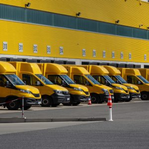 A fleet of yellow trucks are all lined up in a row in a parking lot in front of a yellow building.