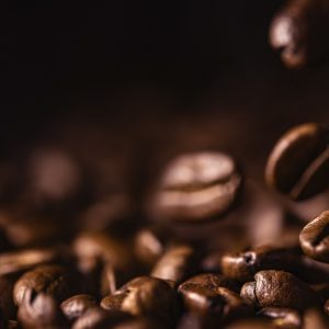 A close-up of coffee beans falling onto a table. The background is brown, and the beans are whole and intact.