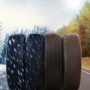 Four tires displayed on a road with winter snow on the left transitioning to an autumn landscape on the right.