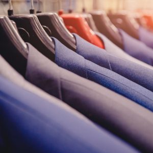 A close-up of multiple black, grey, and blue suit jackets on individual hangers next to each other on a rack.