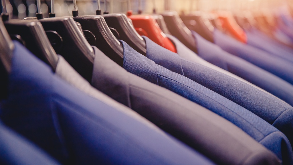 A close-up of multiple black, grey, and blue suit jackets on individual hangers next to each other on a rack.