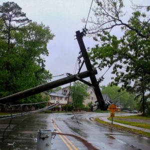 A telephone pole has been knocked over and stretches across a two-lane residential road. A home is seen behind the pole.