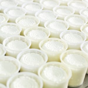 A close-up of multiple rows of cottage cheese in clear plastic packaging on a stainless steel surface.