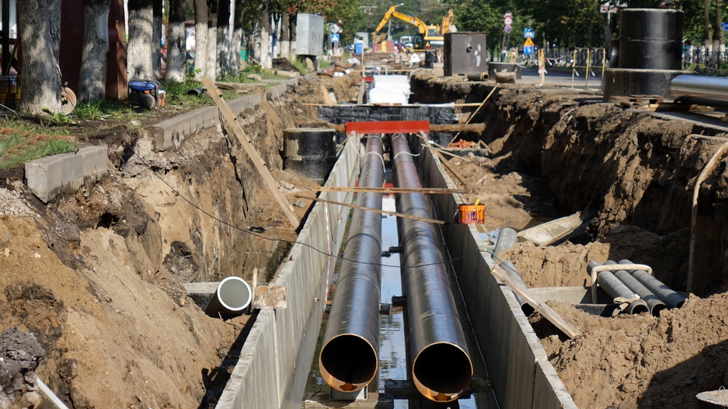 A ditch is dug out along a city street. There are two long pipes running parallel with each other that are uncovered.