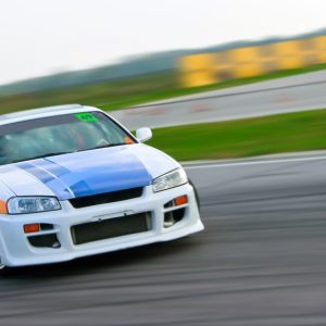 A blue and white race car drifts on a race track. The green grass lies behind it, along with another roadway.