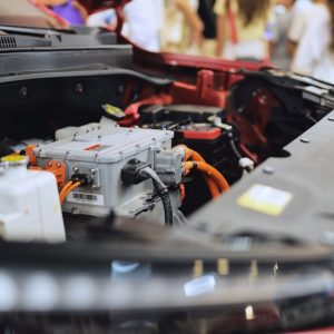 A red car with its hood open at an automotive exhibition. Many connectors are hooked up to the hardware under the hood.