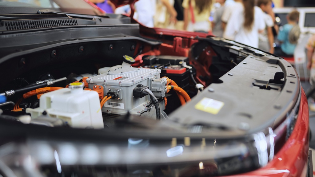 A red car with its hood open at an automotive exhibition. Many connectors are hooked up to the hardware under the hood.