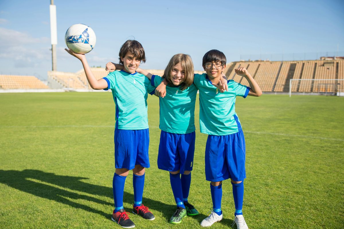 three kid soccer players pose for camera holding a soccer ball