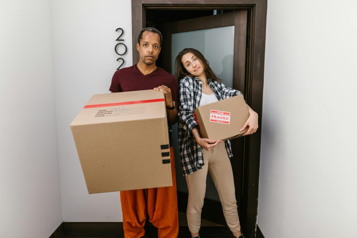 couple friends holding boxes outside of an apartment door