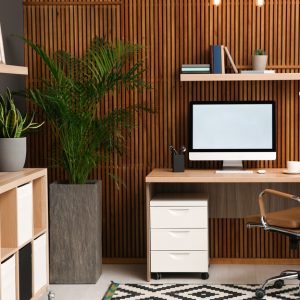 A stylish work-from-home setup with a wooden desk, ergonomic chair, desktop computer, and indoor plants in a well-lit home office.