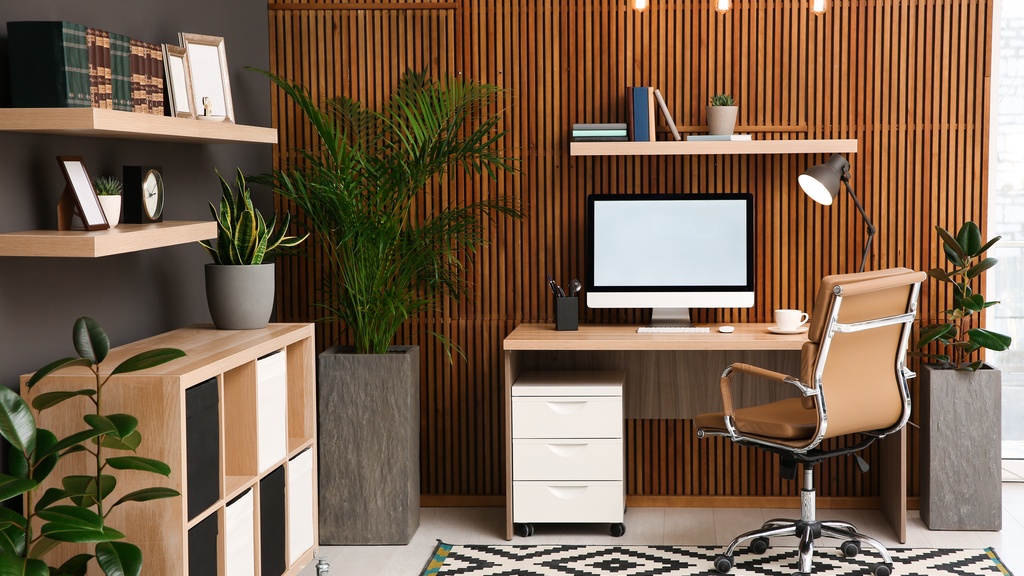 A stylish work-from-home setup with a wooden desk, ergonomic chair, desktop computer, and indoor plants in a well-lit home office.
