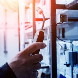 A technician uses a handheld electronic leak detector near insulated industrial HVAC equipment and wiring in a facility.