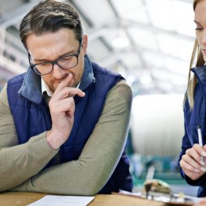 A man and woman looking at a slip of paper that's sitting on a cardboard box. The woman has a clipboard and pen in hand.