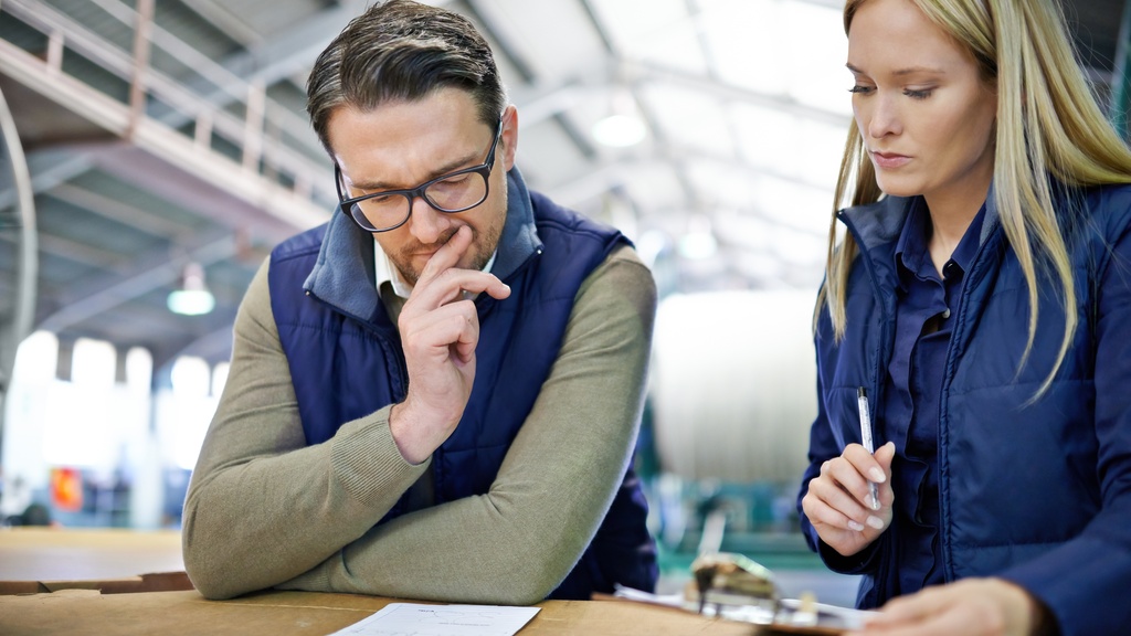 A man and woman looking at a slip of paper that's sitting on a cardboard box. The woman has a clipboard and pen in hand.