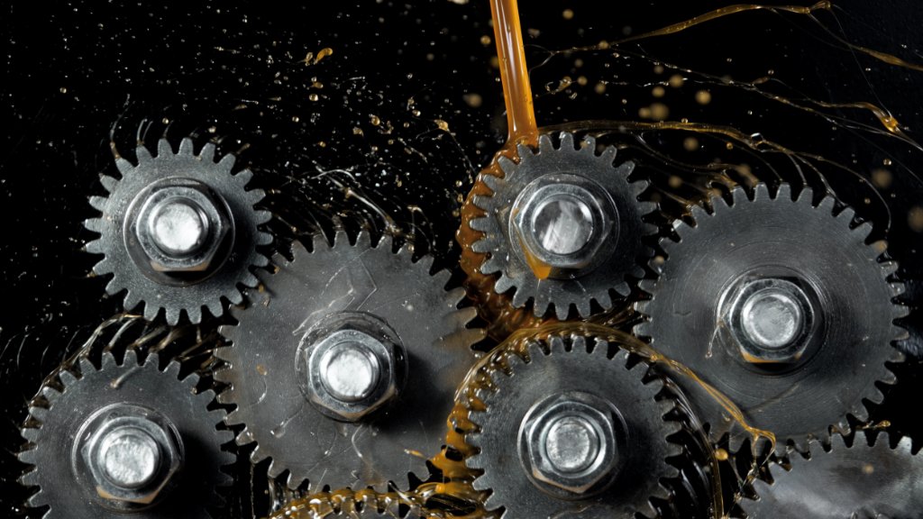 Multiple tooth gear wheels are spinning. Gear oil is spilled onto the gears and splattered against a black background.