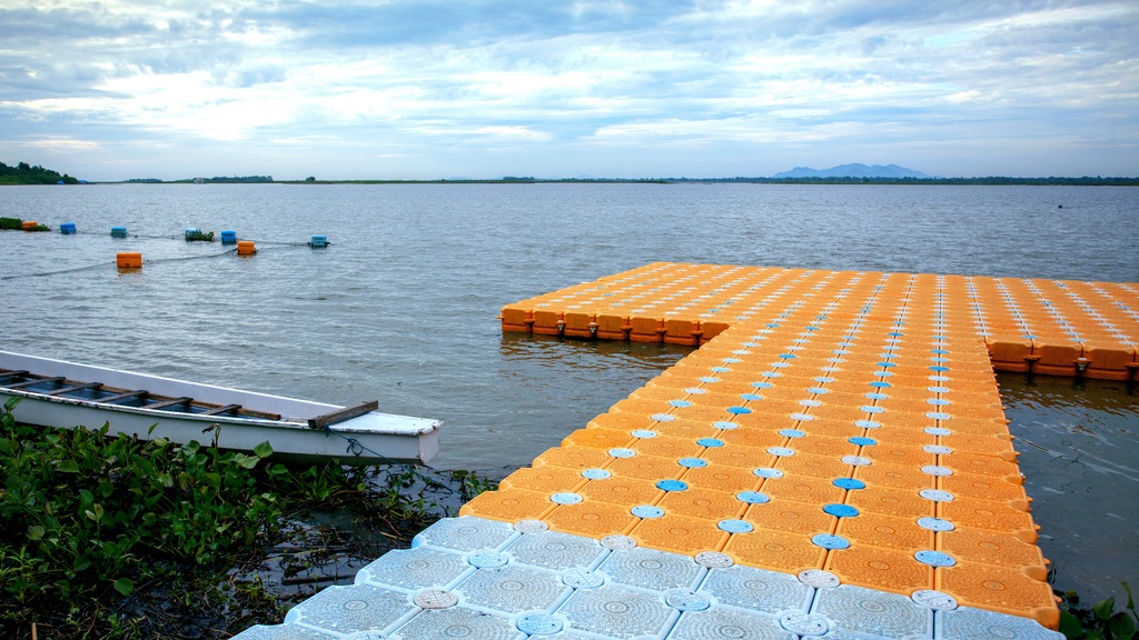 A blue and orange plastic floating dock on a shore with a canoe next to it and shoreline in the background.
