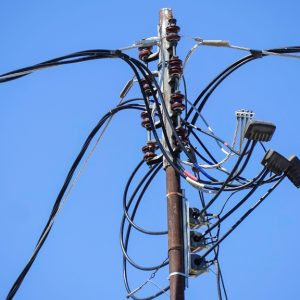 An old power pole with multiple utility lines running across it and intersecting in different areas.