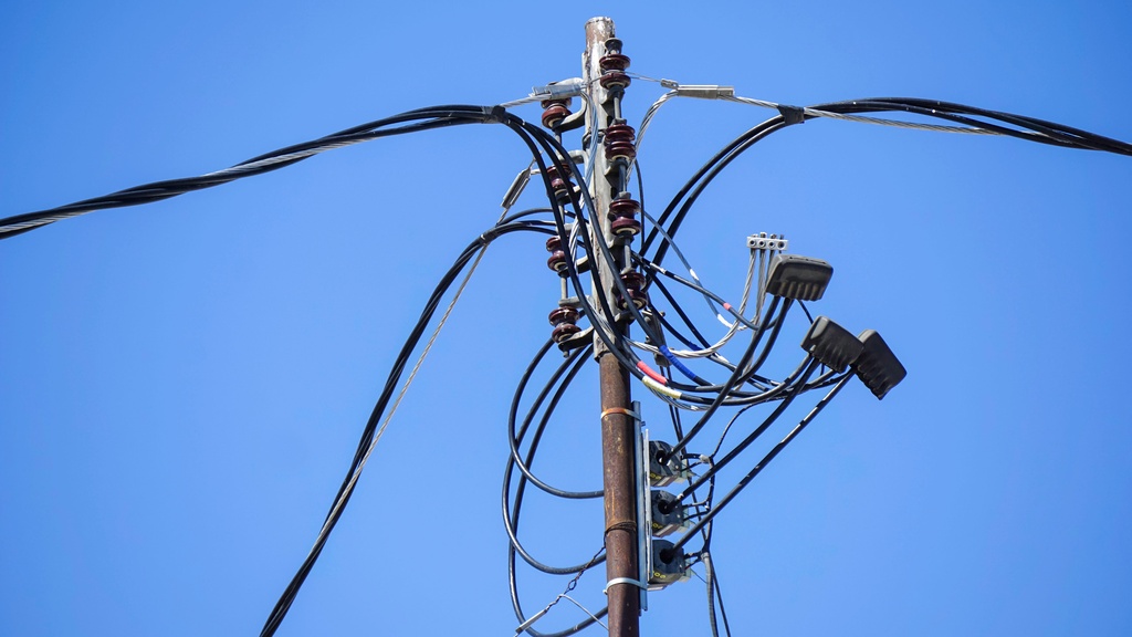 An old power pole with multiple utility lines running across it and intersecting in different areas.