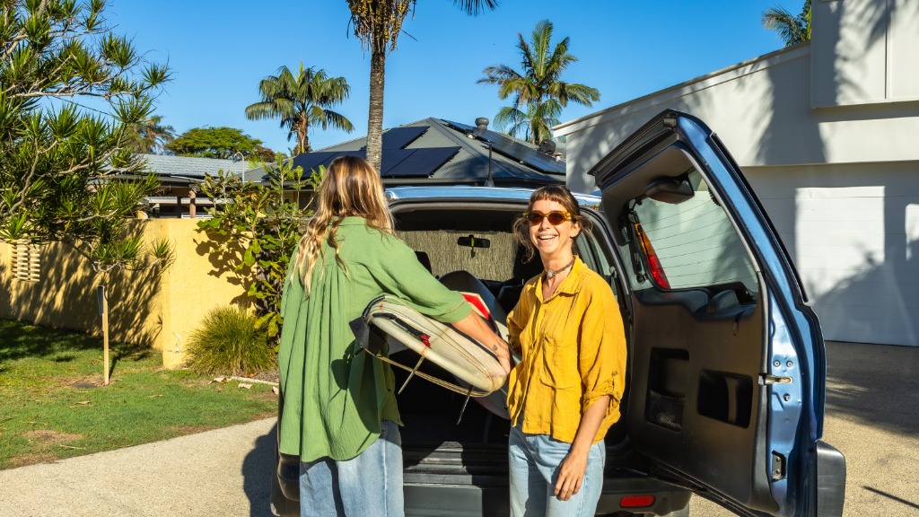 Two women are standing behind a hatch-back car with he hatch open. One woman is looking at the camera.