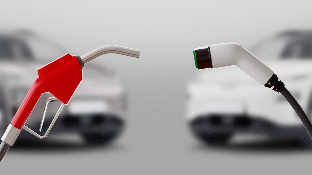 A red gasoline nozzle and electric vehicle charging plug facing each other with blurred cars in the background.
