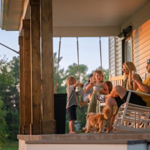 A family with three children and a small dog sitting on the front porch of their home on a sunny day.