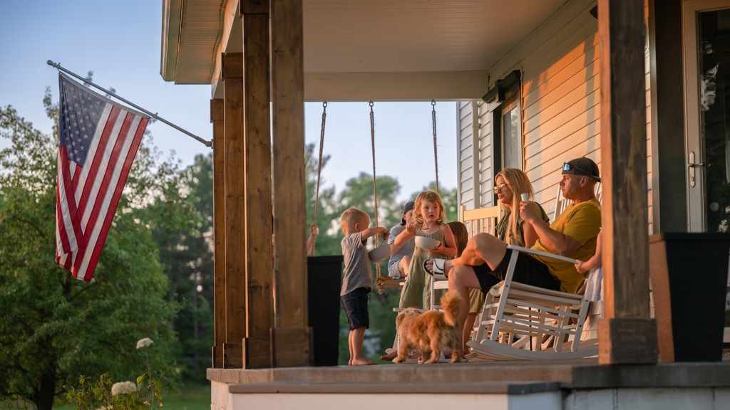 A family with three children and a small dog sitting on the front porch of their home on a sunny day.