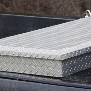 A close-up of a large, silver toolbox resting across the back of a truck bed. The truck is black.
